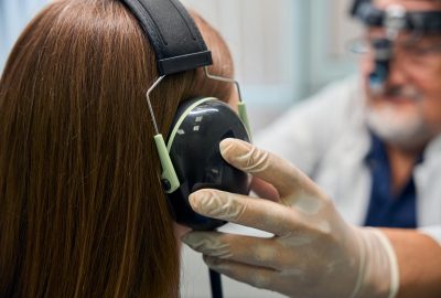 Gloved hand of a doctor adjusting the headphones on a patients head during an examination