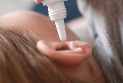 Mother dripping medication into daughter's ear on blurred background, closeup